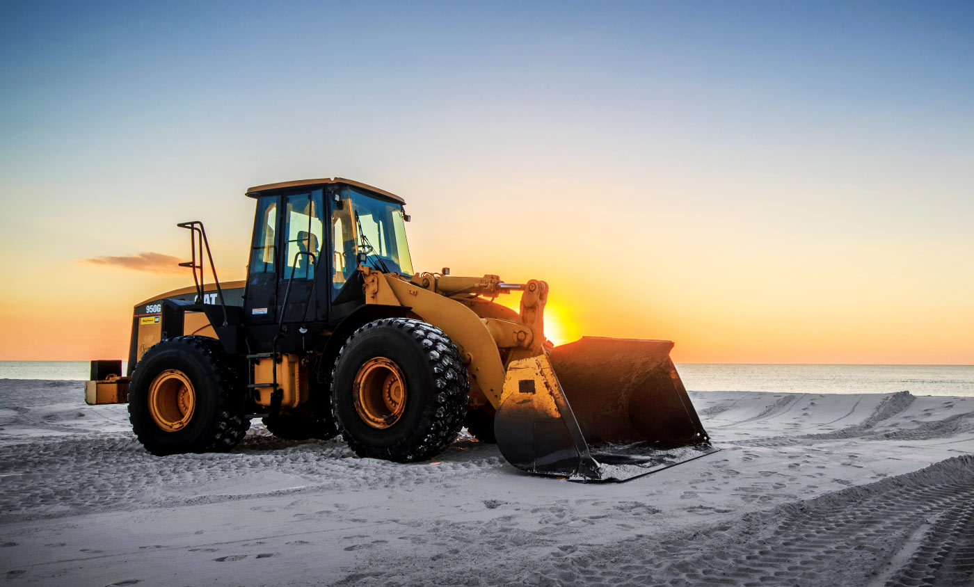 A bulldozer on the beach at sunset.