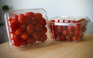 Tomatoes in plastic containers on a wooden table.