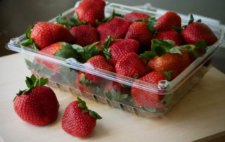 A bunch of strawberries in a plastic container on a table.