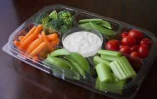 A plastic container filled with vegetables and dip.